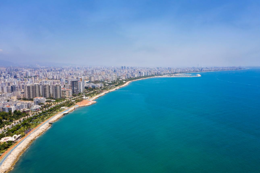 An aerial view of Mersin featuring the city skyline along the Mediterranean coast and harbor.