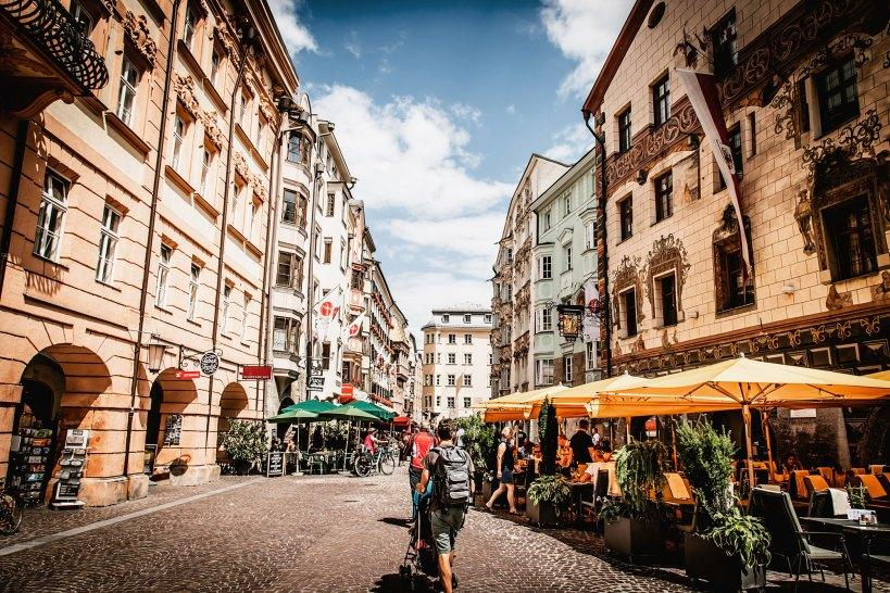 People walking through streets in Austria with shops, cafés, and historic architecture.