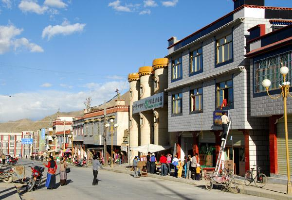 People walking through Shigatse streets with local shops, cafés, and market activity.