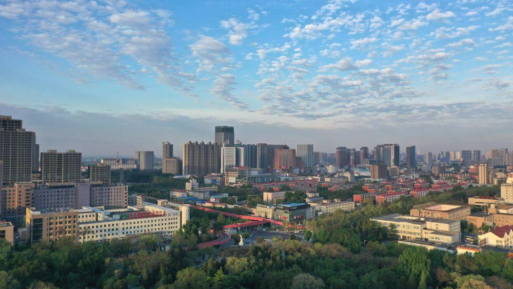 An aerial view of Tangshan showing the city skyline with urban buildings and nearby mountains.