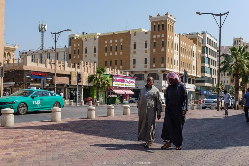 People walking through Dammam streets with shops, cafés, and local market activity.