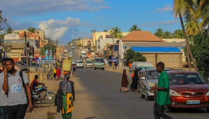 People walking along a busy street lined with shops, market stalls, and colorful buildings in central Nampula.