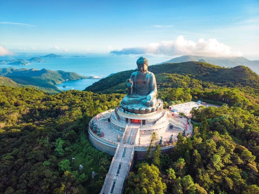 Panoramic view of the bronze Buddha, surrounding mountains, and visitors ascending the steps.