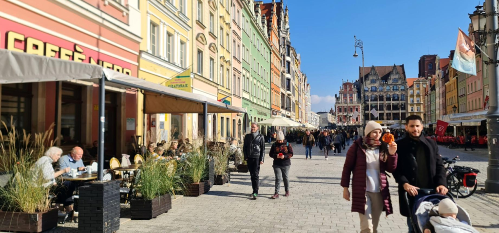 People walking through Wrocław streets with shops, cafés, and local market activity.