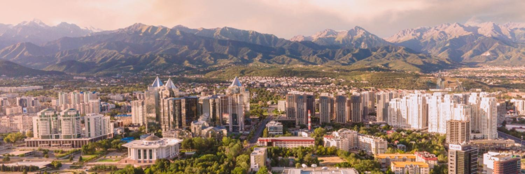 An aerial view of Almaty showing the city skyline with the Tian Shan mountains in the background.