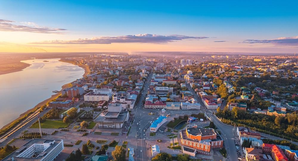 A panoramic aerial view of Tomsk showing the cityscape along the Tom River and historic wooden architecture in Siberia, Russia.