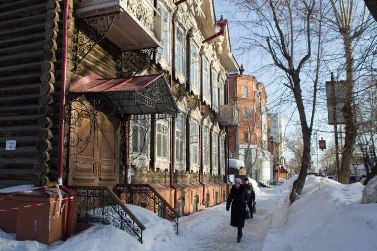 Visitors walking through streets in Tomsk with local shops, cafés, pedestrians, and traditional wooden houses.