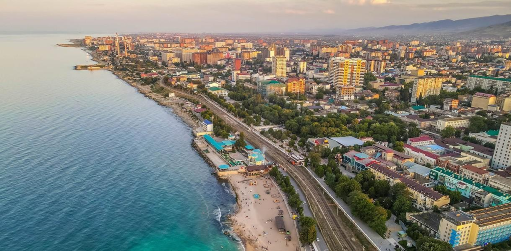 A panoramic aerial view of Makhachkala showing the cityscape, Caspian Sea coastline, and surrounding mountains in Russia