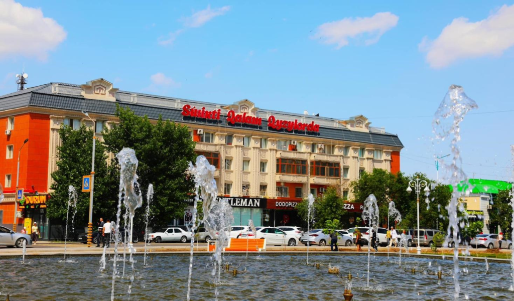 People walking through Kyzylorda streets with shops, cafés, and local market activity.
