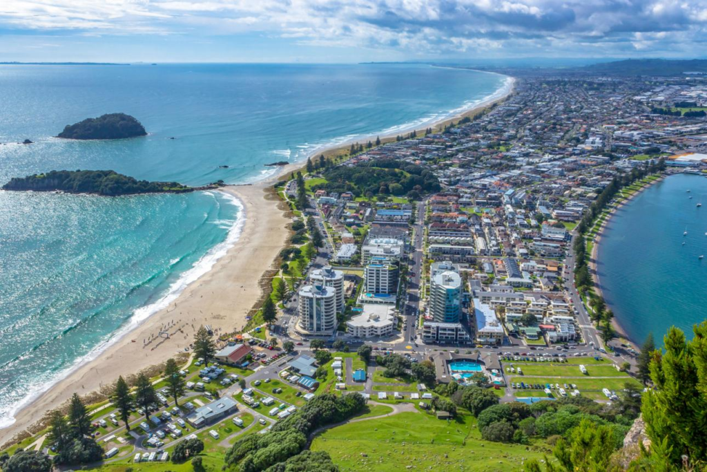 An aerial view of Tauranga showing the city skyline with Mount Maunganui and coastline in the background.