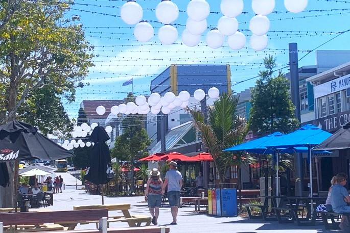 People walking through Tauranga streets with shops, cafés, and local market activity.