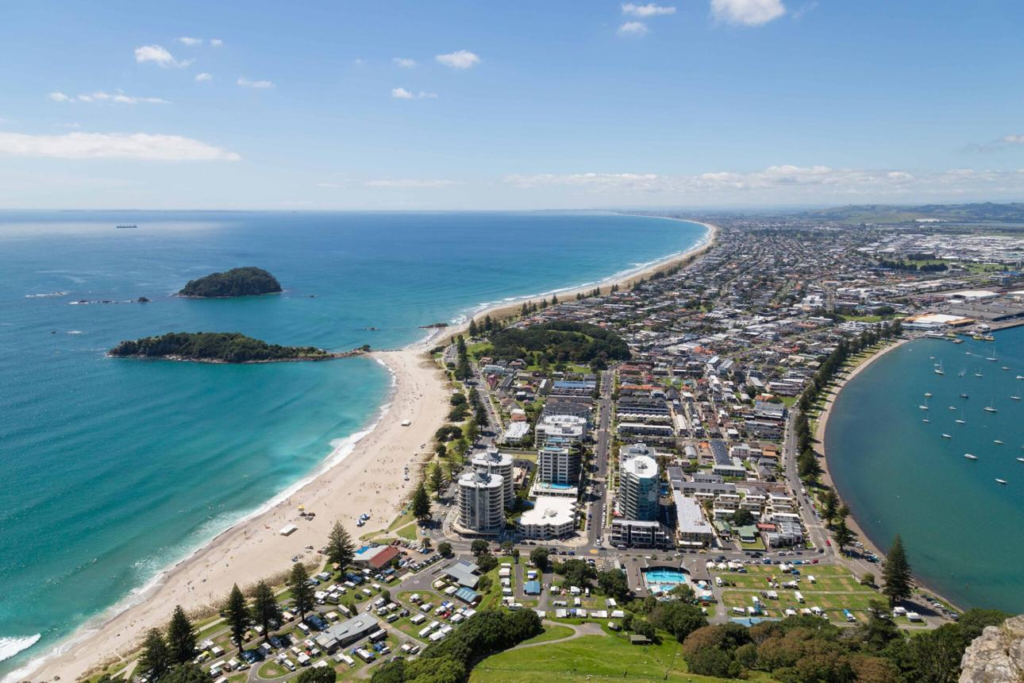 Tourists enjoying Mount Maunganui beach in Tauranga with city and coastal views.