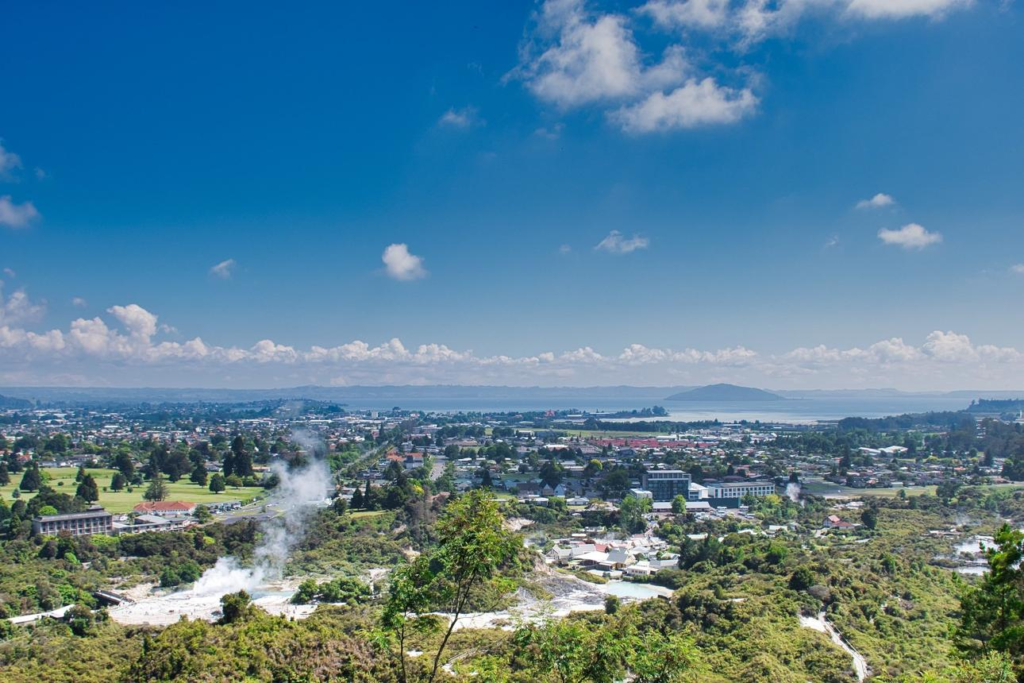 An aerial view of Rotorua showing the city skyline, geothermal features, and surrounding lakes.