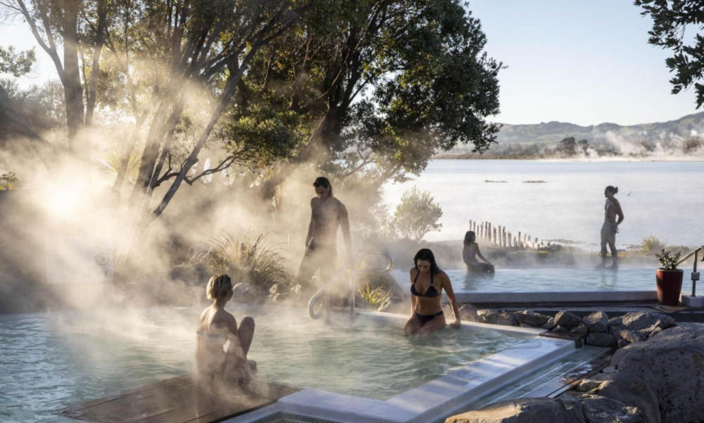 Tourists enjoying the geothermal pools at the Polynesian Spa in Rotorua with surrounding hills.