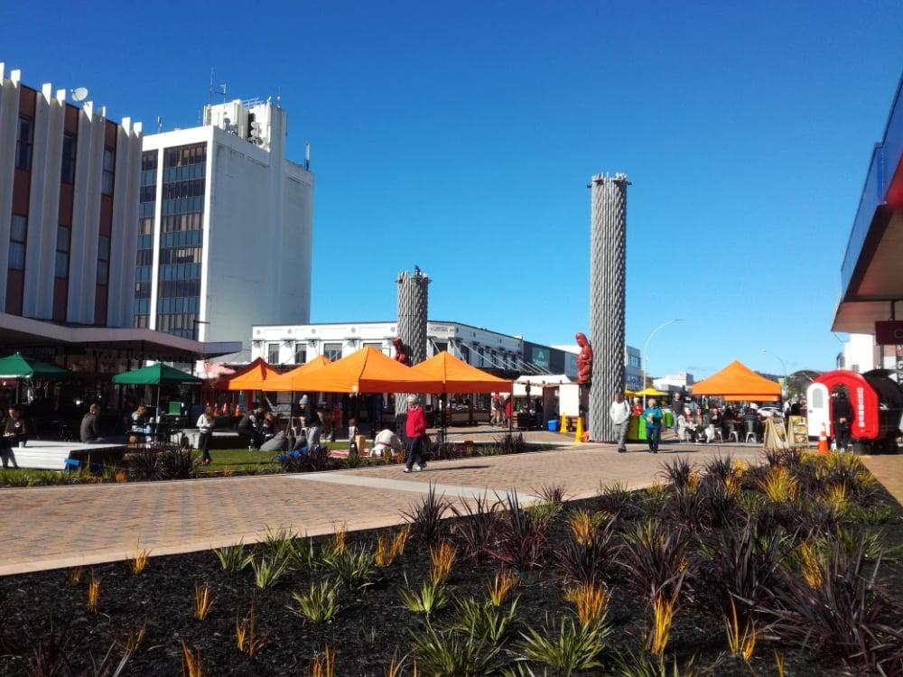 Locals and visitors exploring a bustling market in Rotorua with shops, stalls, and Maori cultural elements.