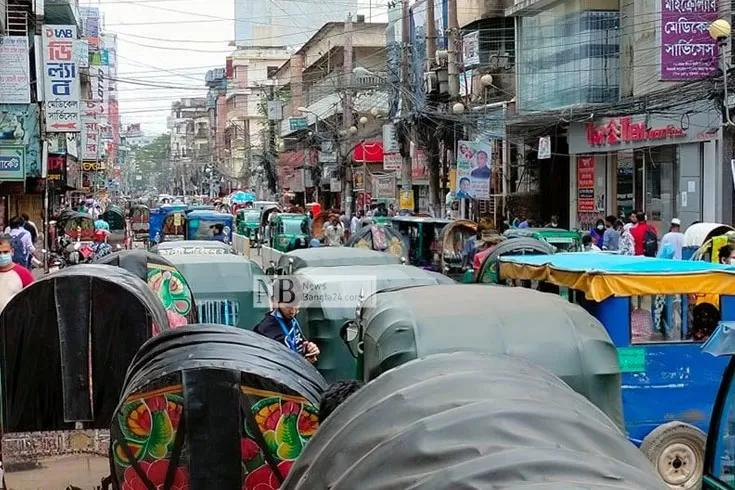 People walking through Barishal streets with shops, cafés, and local market activity.