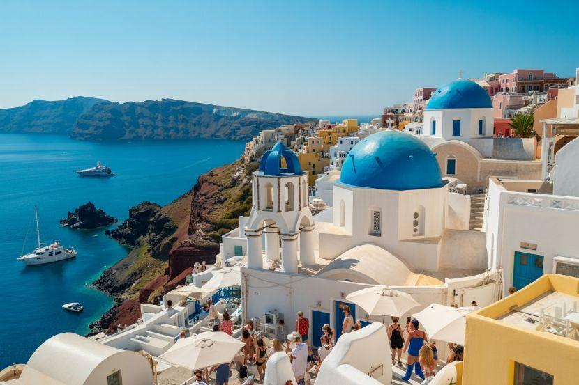 Tourists exploring white buildings with blue domes on Santorini overlooking the Aegean Sea