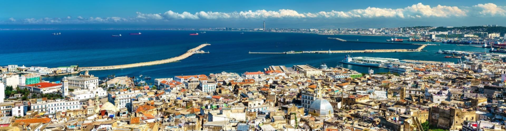 A panoramic view of Algiers overlooking the Mediterranean Sea with white buildings climbing the hillside.