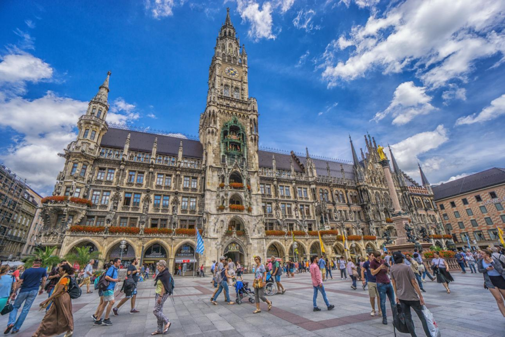 Visitors walking through Marienplatz beside the New Town Hall on a sunny afternoon.