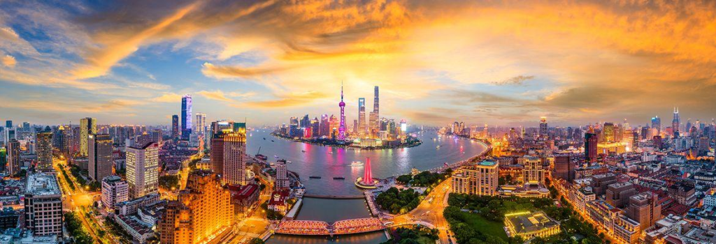 A panoramic view of Shanghai's skyline with modern skyscrapers beside the Huangpu River at sunset.