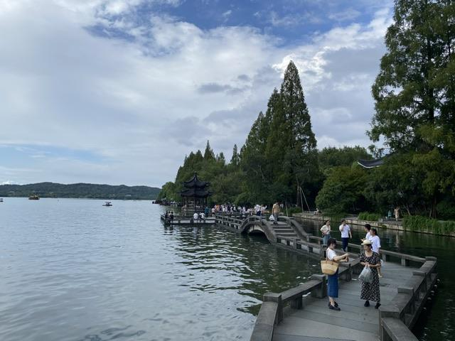Visitors walking beside West Lake with traditional bridges, trees, and calm water.