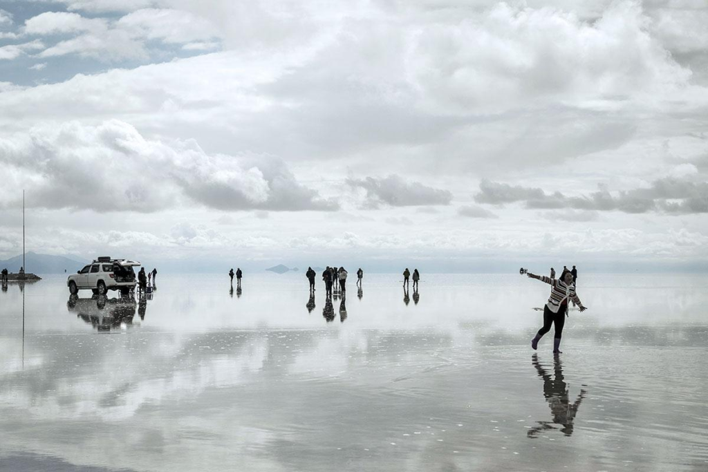 Visitors walking across the reflective surface of Salar de Uyuni beneath a wide blue sky.
