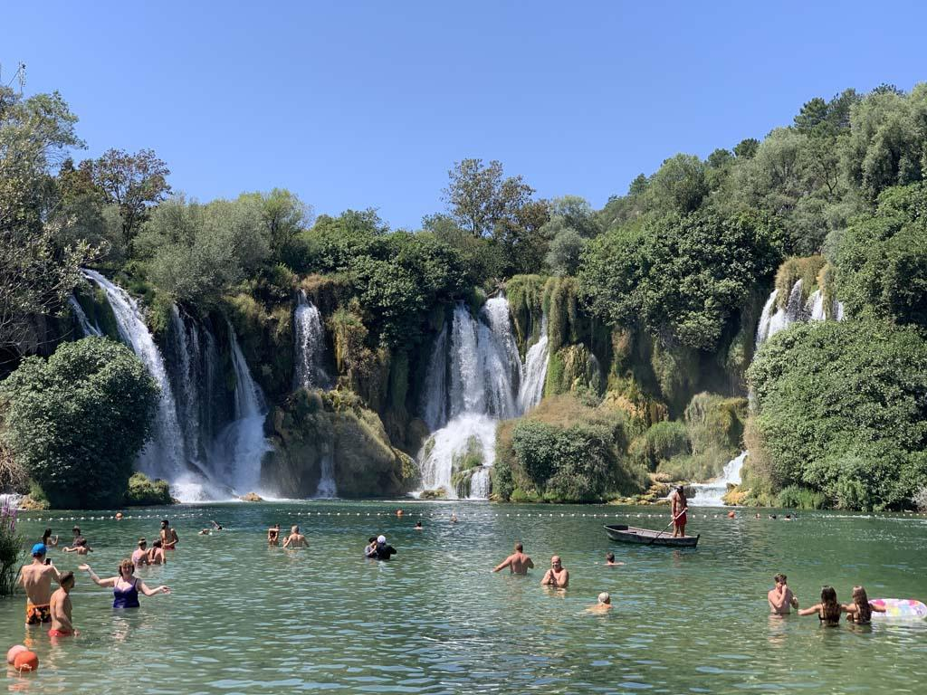 Visitors enjoying the turquoise pools beneath Kravica Waterfalls surrounded by lush greenery.