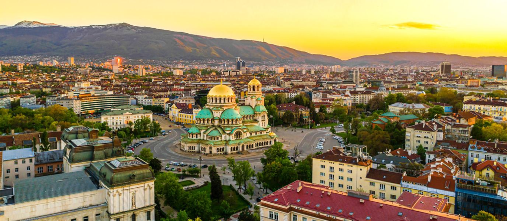 A panoramic view of Sofia featuring the Alexander Nevsky Cathedral with mountains in the distance.