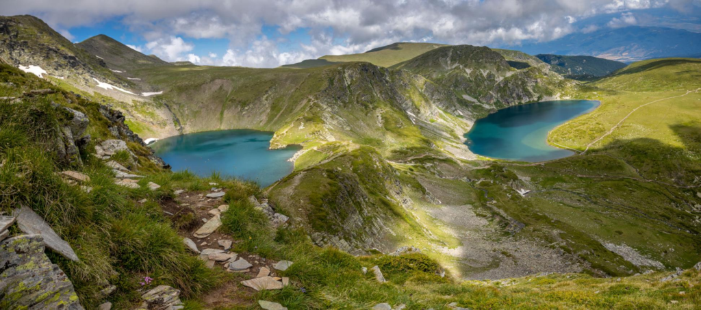 Crystal-clear mountain lakes surrounded by grassy slopes and rocky peaks in the Rila Mountains.
