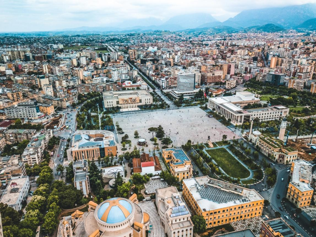 A panoramic view of Tirana featuring colorful buildings, Skanderbeg Square, and surrounding hills.
