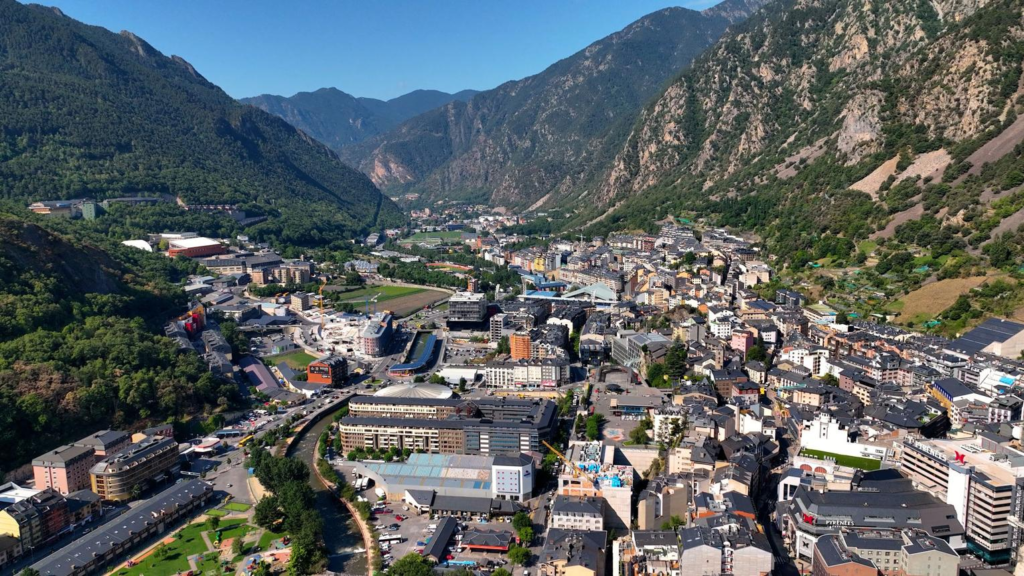 A panoramic view of Andorra la Vella surrounded by the forested peaks of the Pyrenees Mountains.