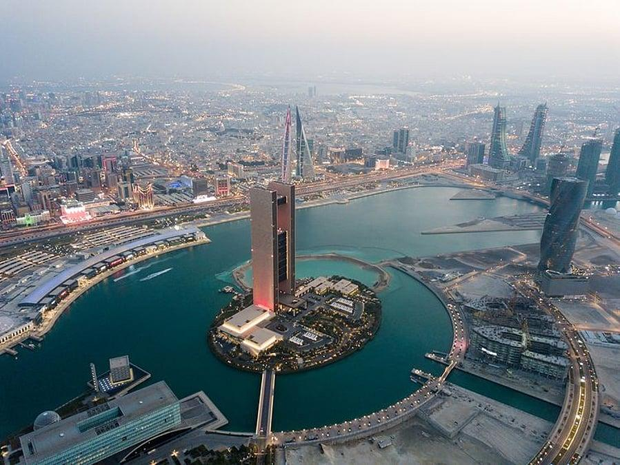 A panoramic view of Manama's modern skyline overlooking Bahrain Bay at sunset.